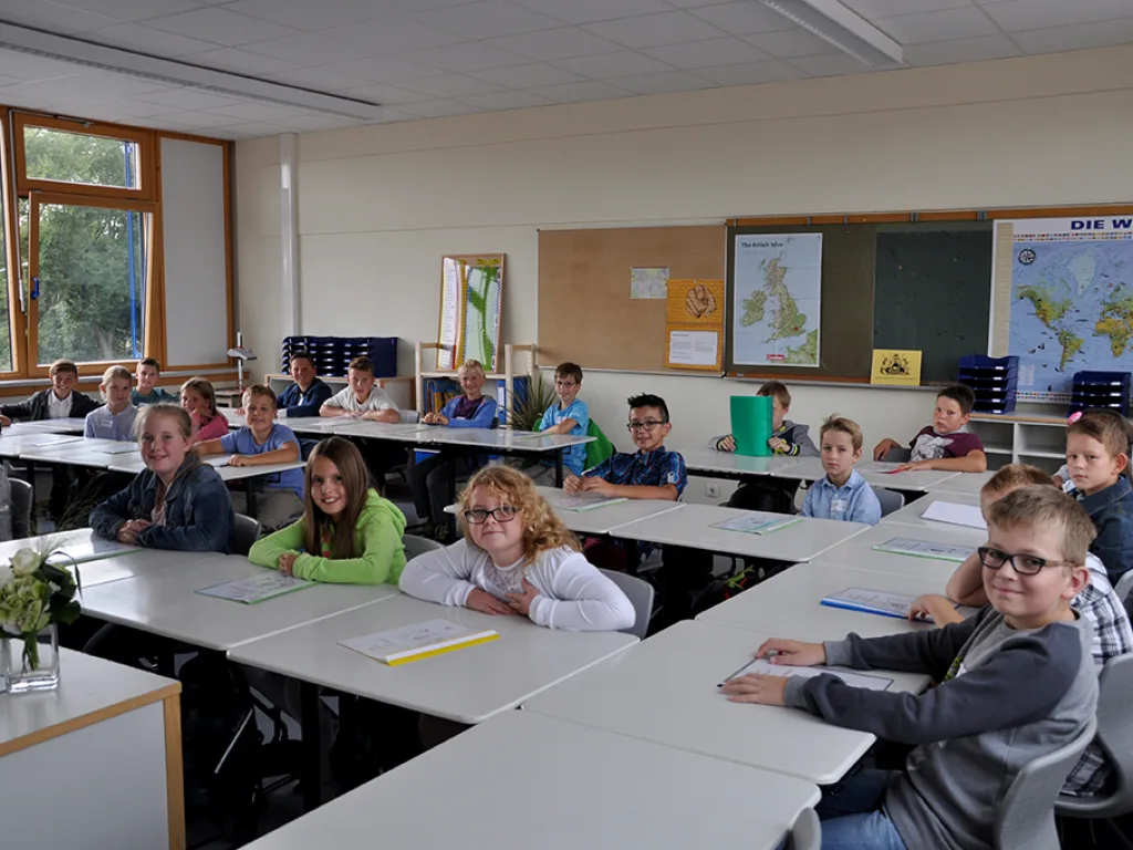 Kinder sitzen an Gruppentischen im Klassenraum.